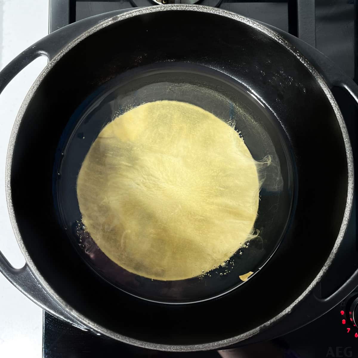 Placing a papad in hot oil in a black saucepan.