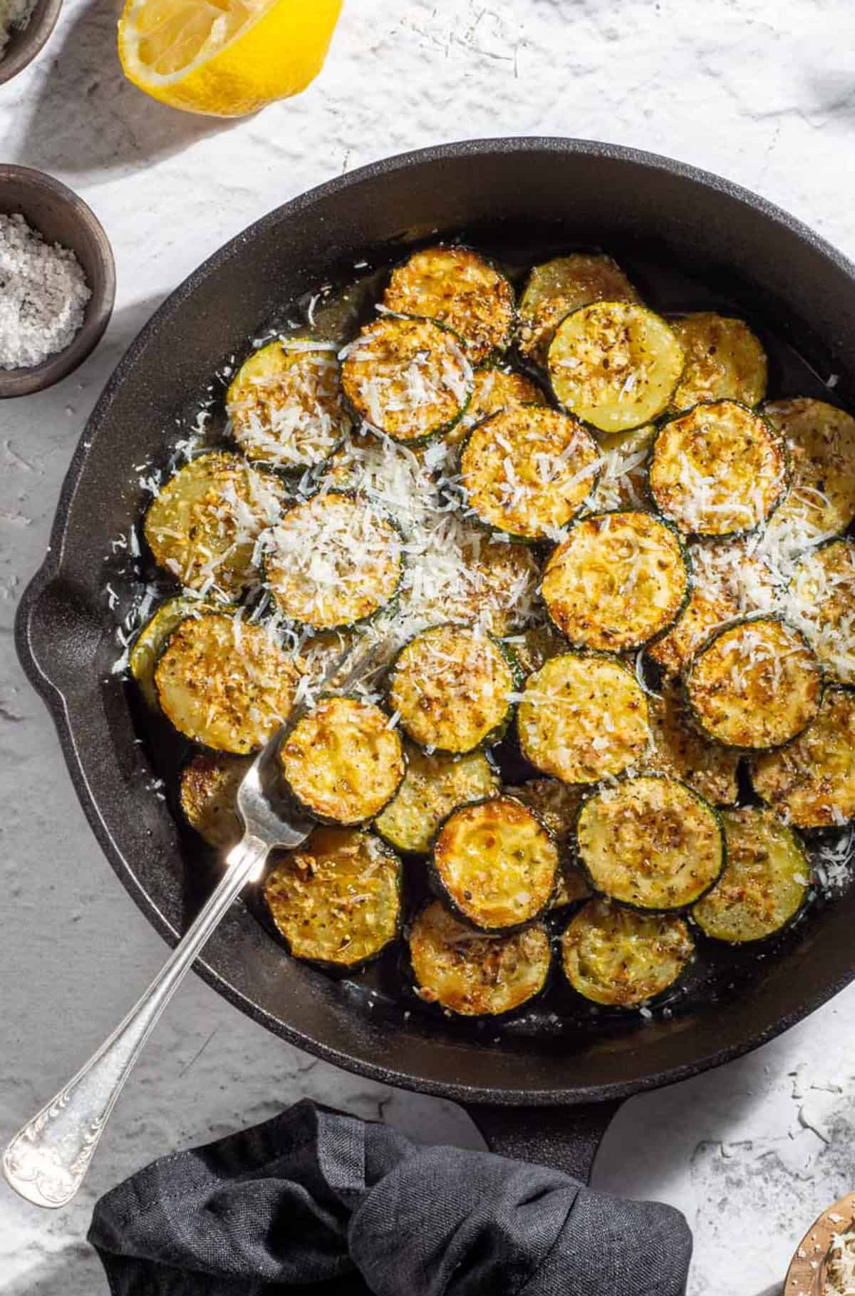 Pan-fried courgette slices with garlic, lemon and Parmesan in a cast-iron frying pan.