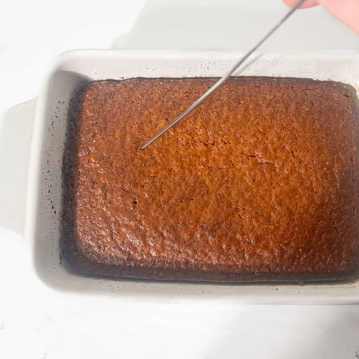 Poking holes into the baked malva pudding.