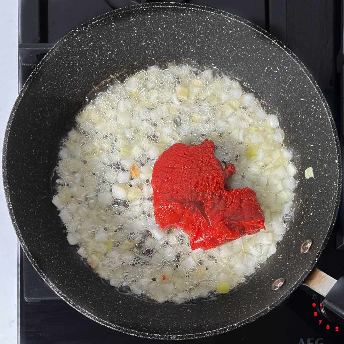 Adding tomato paste to the fried onions.