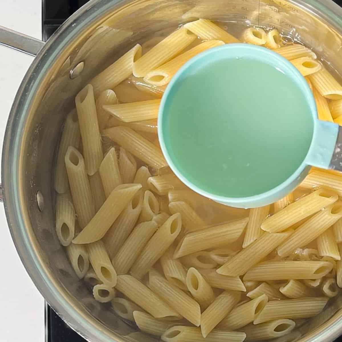 Scooping pasta water from the pasta before draining it.