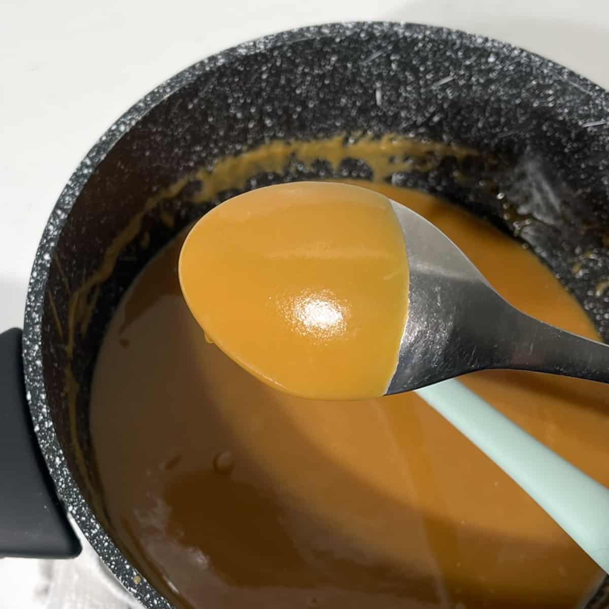 Showing the surface texture of the caramel sauce on the back of a metal spoon.