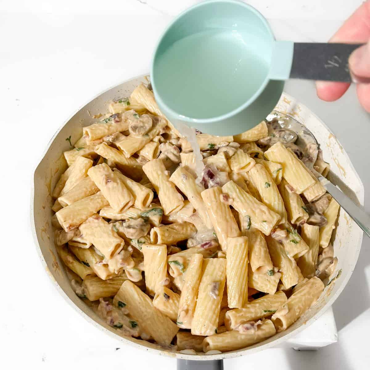 Adding the reserved pasta water to the creamy steak pasta.
