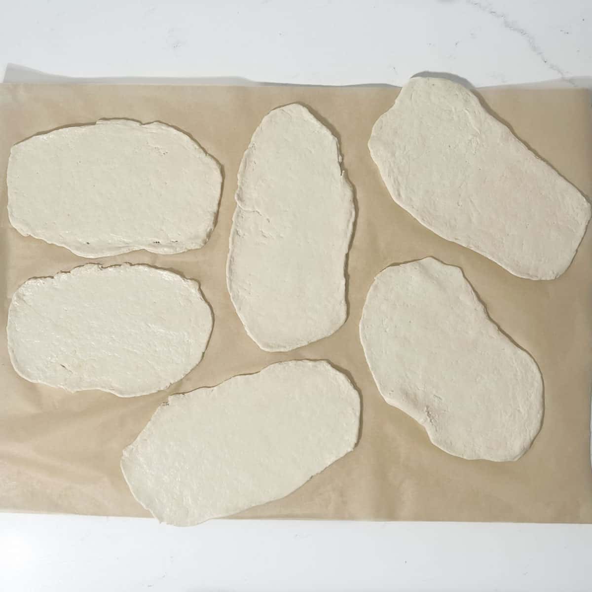 Rolled out flatbreads on baking paper.