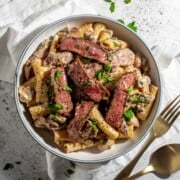 A bowl of creamy steak pasta on a white background.