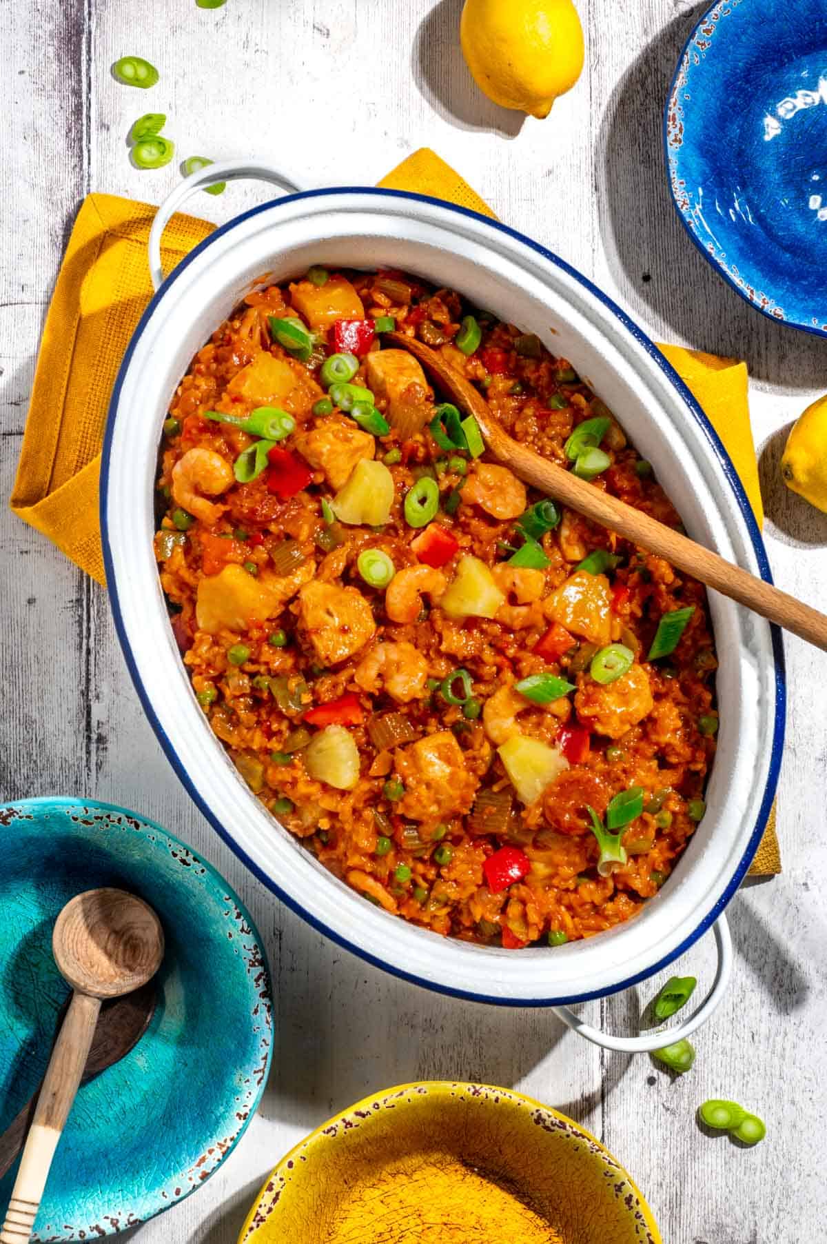 Chicken and chorizo jambalaya in a large, white oval pot surrounded by colourful bowls.