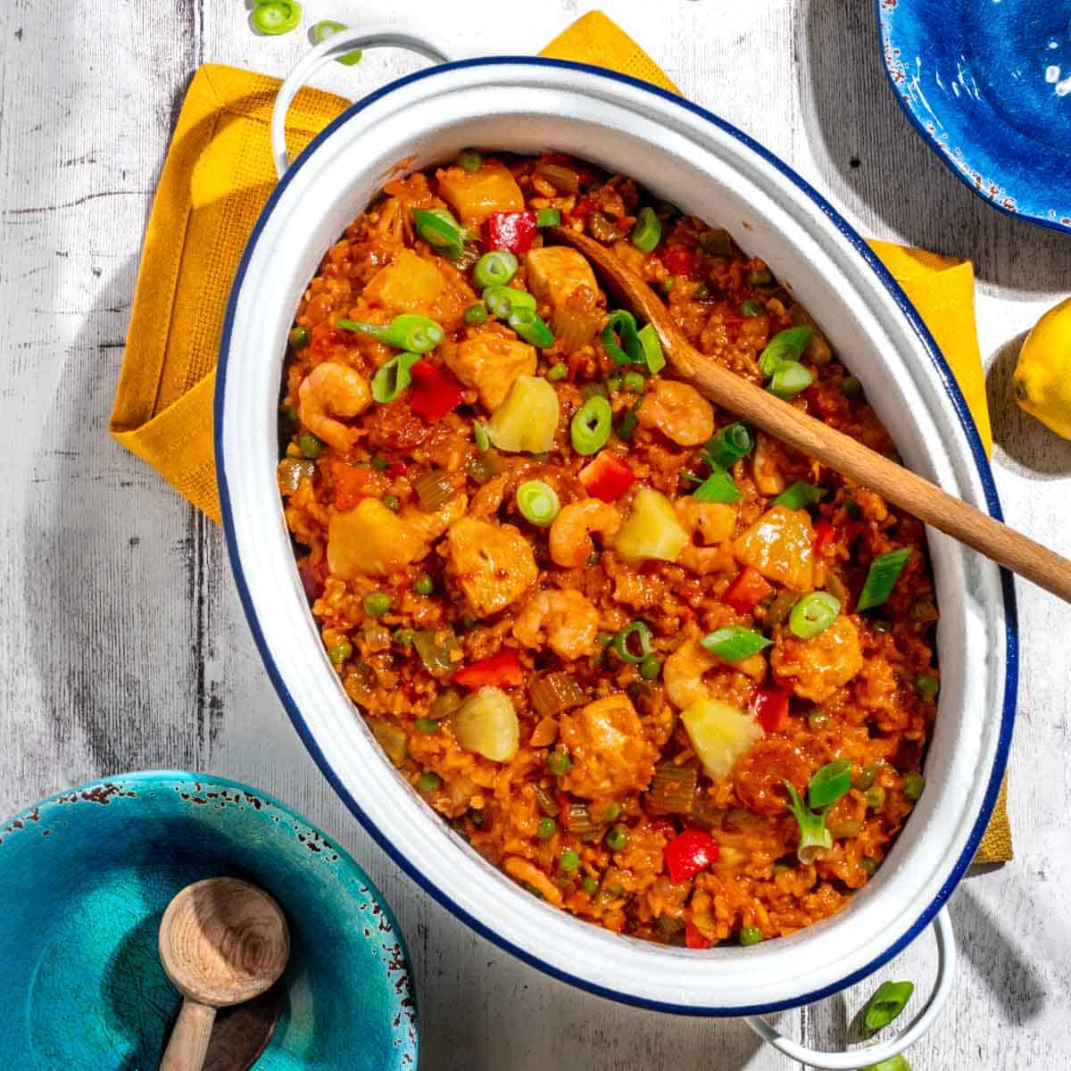 Chicken and chorizo jambalaya in a large, white oval pot surrounded by colourful bowls.