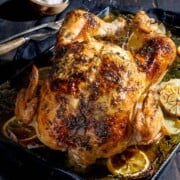Whole Greek roast chicken on a baking tray.