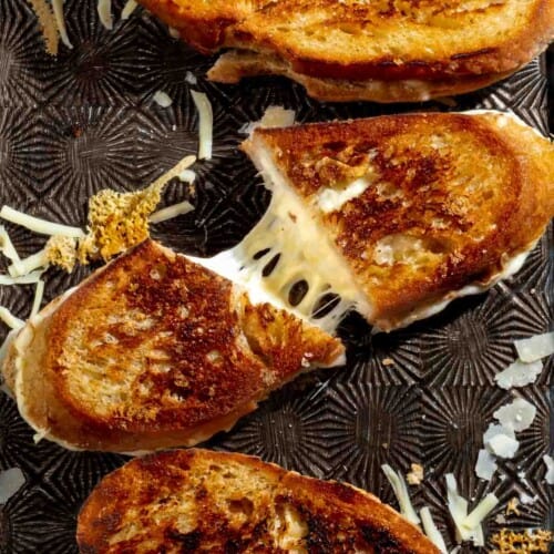 Sourdough grilled cheese sandwich sliced and pulled apart to show melted cheese inside.