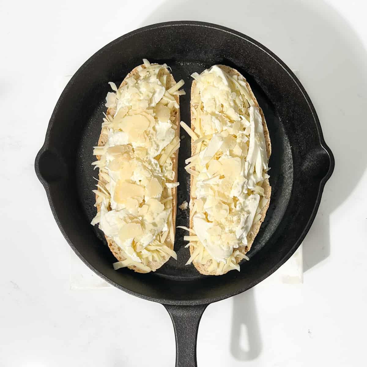 Adding tow slices of bread topped with cheese to a cast iron skillet.