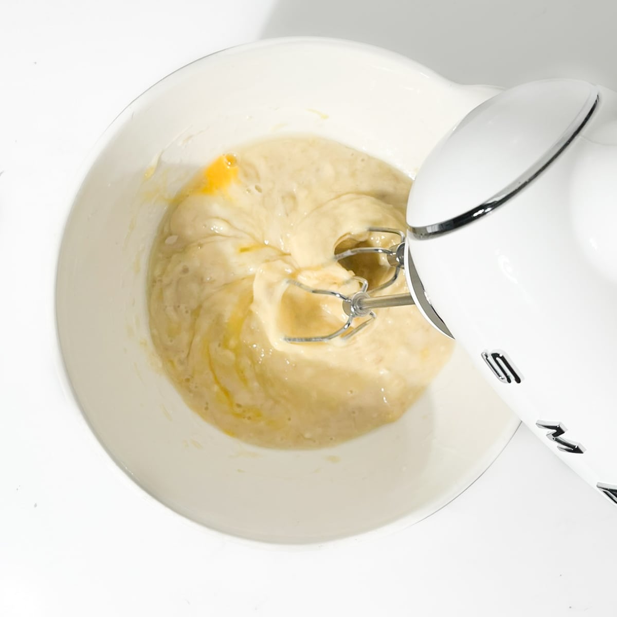 Beating the eggs into the banana mixture with an electric hand mixer.