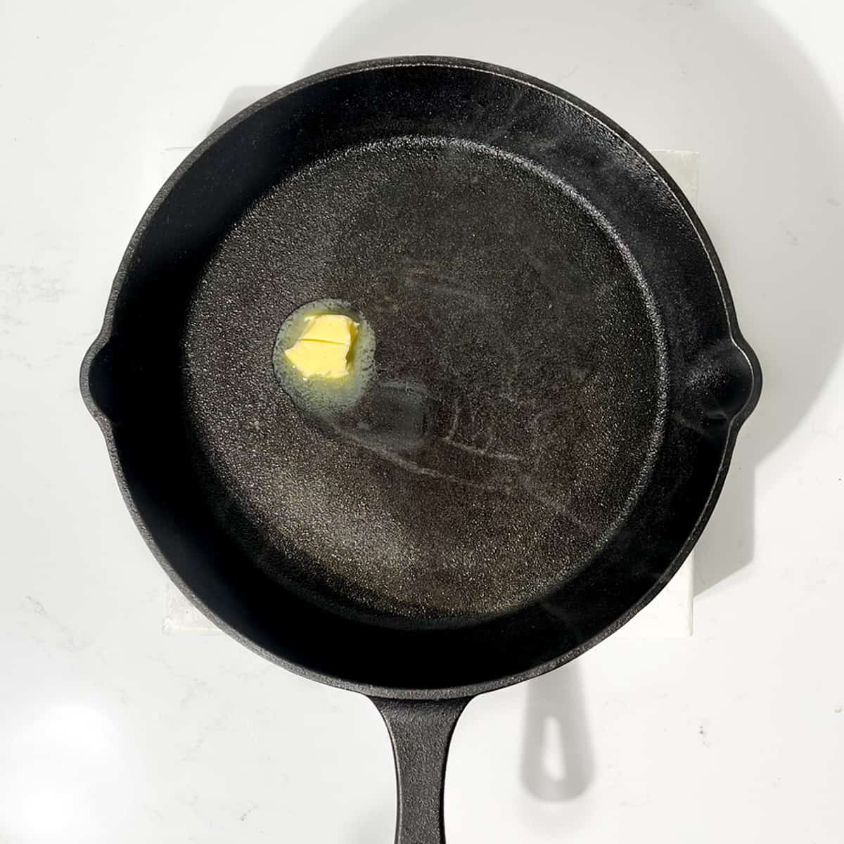Melting a small knob of butter in a cast iron skillet.