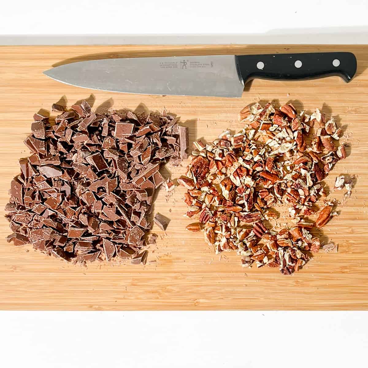 Chopped chocolate and pecan nuts on a chopping board.