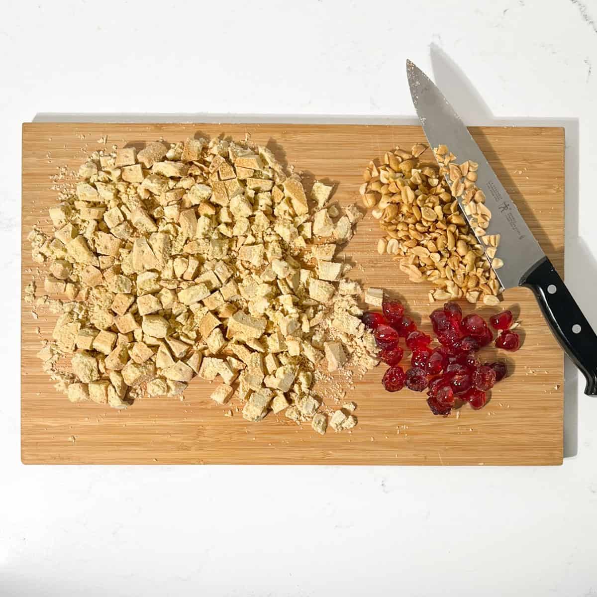 Chopped shortbread, peanuts and glace cherries on a wooden chopping board.