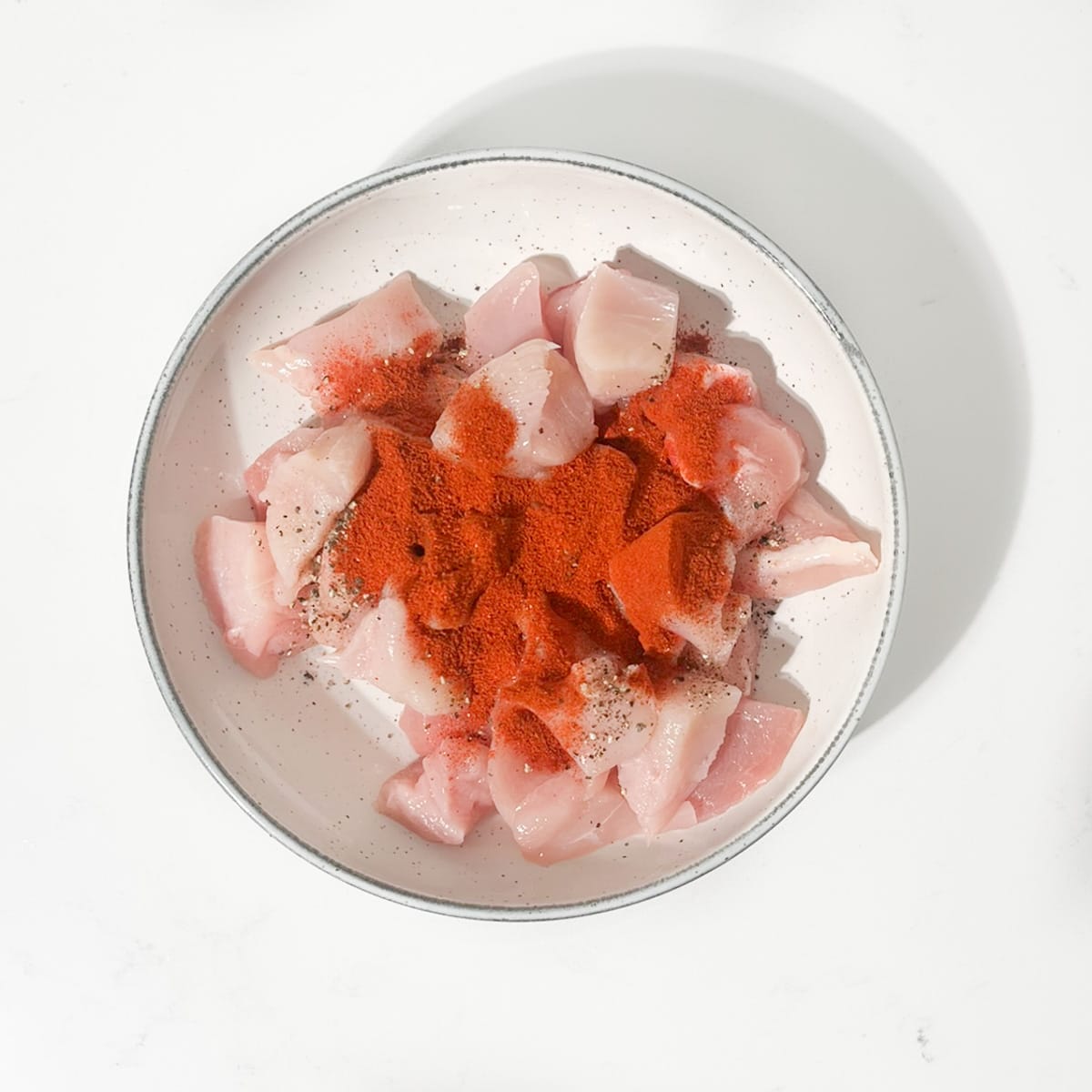 Coating the raw chicken with salt, pepper and smoked paprika in a white bowl.