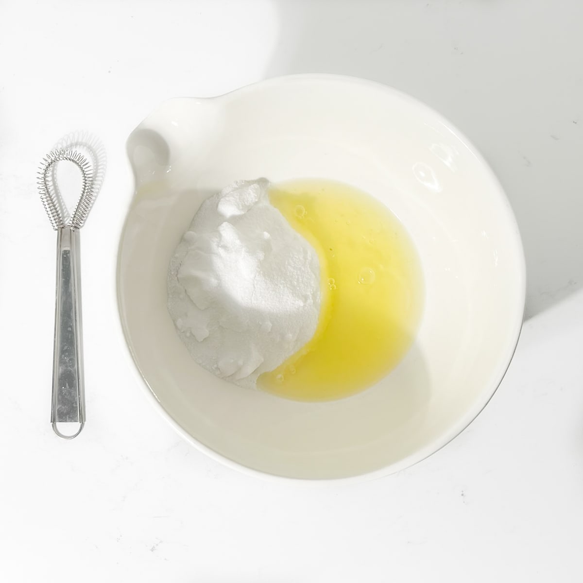 Egg whites and sugar in a white bowl.