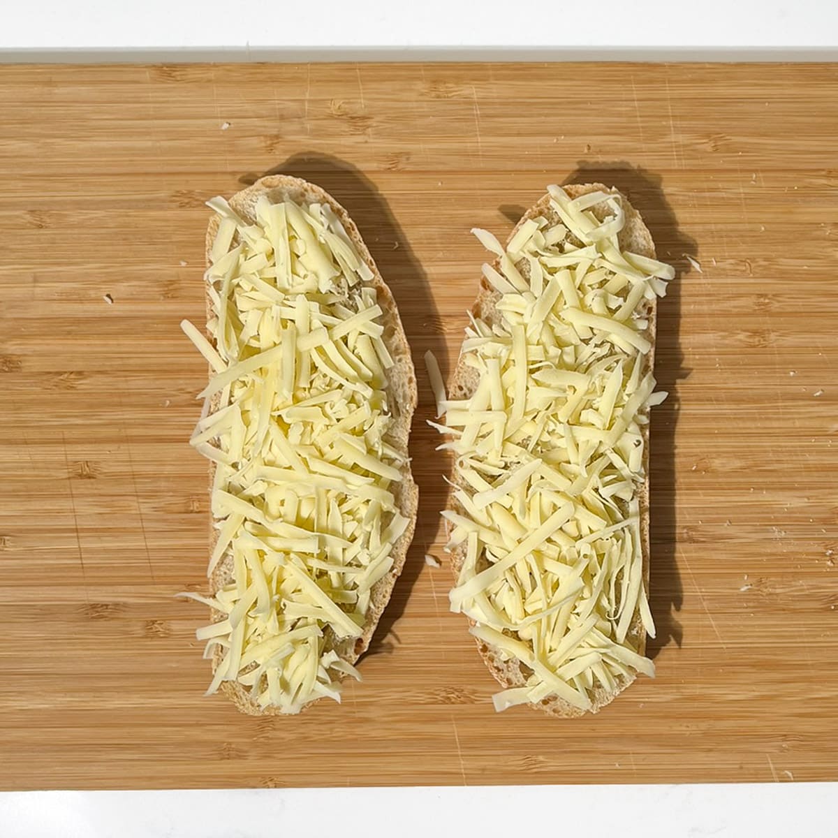 Two slices of bread topped with grated Emmental cheese.