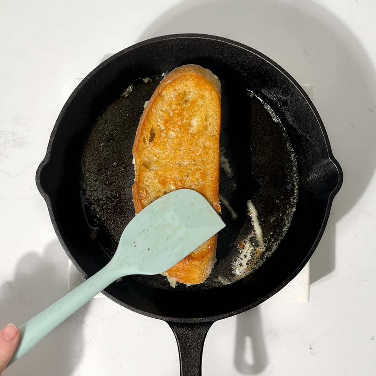 Flipping the sourdough grilled cheese sandwich in a cast iron pan.
