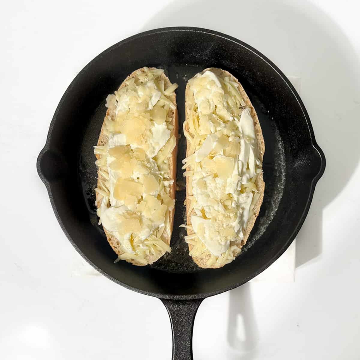 Grilling two slices of sourdough bread topped with cheese in a cast irons pan.