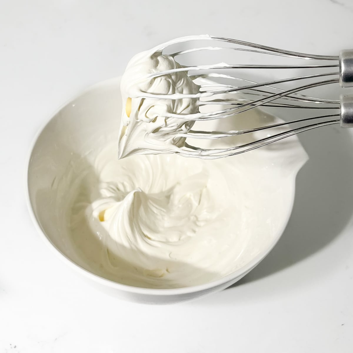Whipping the mascarpone cream to soft peaks with an electric hand mixer.