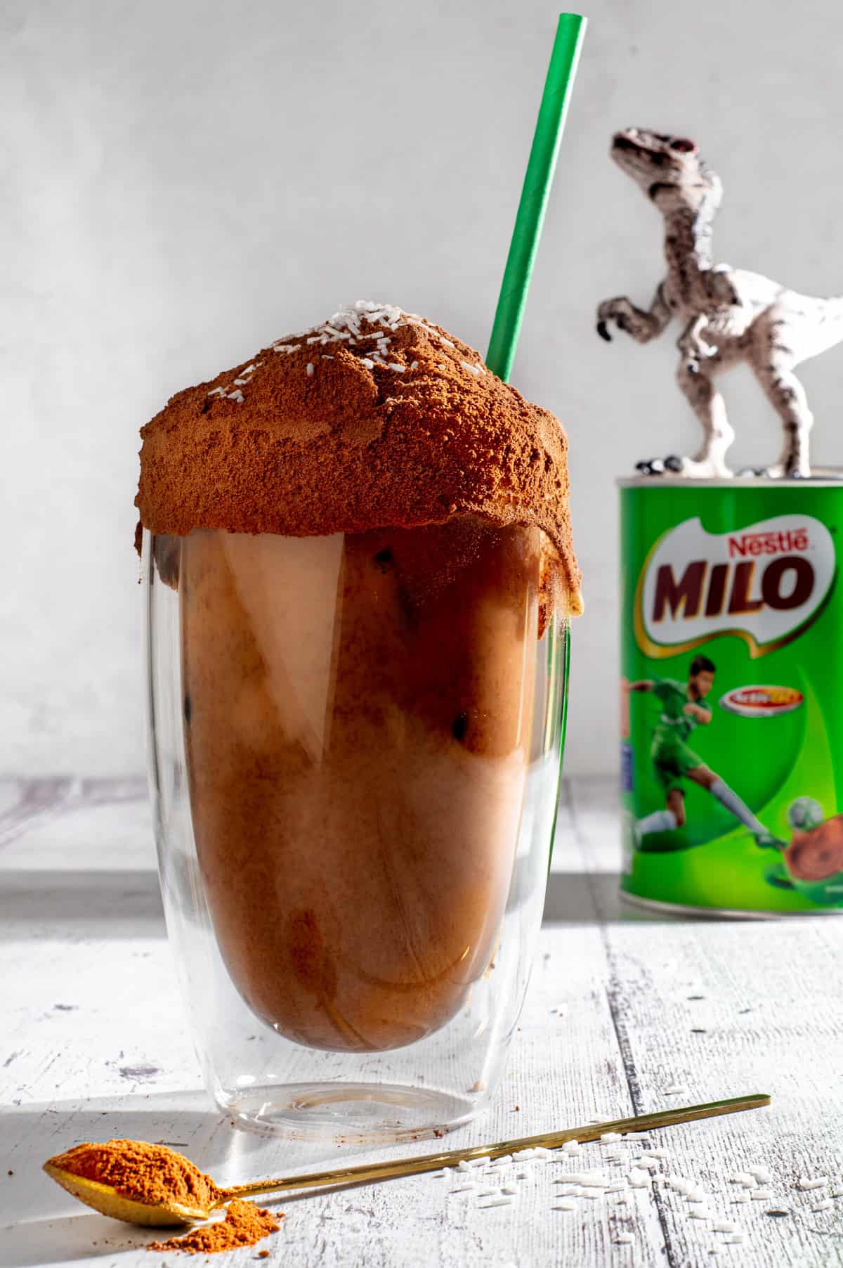 Milo dinosaur next to a tin of Milo and a plastic dinosaur.