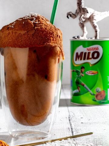 Milo dinosaur next to a tin of Milo and a plastic dinosaur.