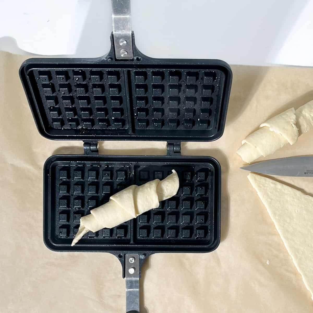 An unbaked, rolled croissant in a waffle pan.