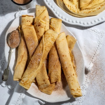 An oval plate of rolled up South African pancakes with cinnamon sugar.
