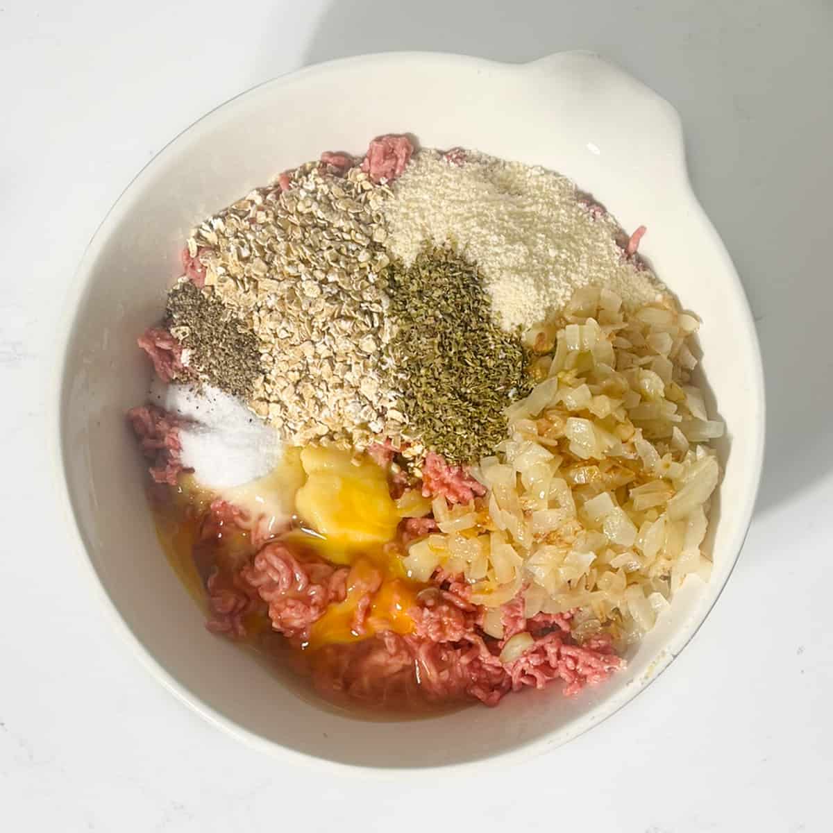 The spices and the oats added to the mince in a large white bowl.