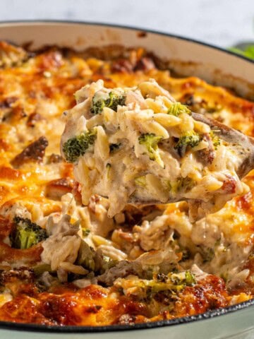 Chicken orzo pasta bake in a round, light green oven dish on a white background.