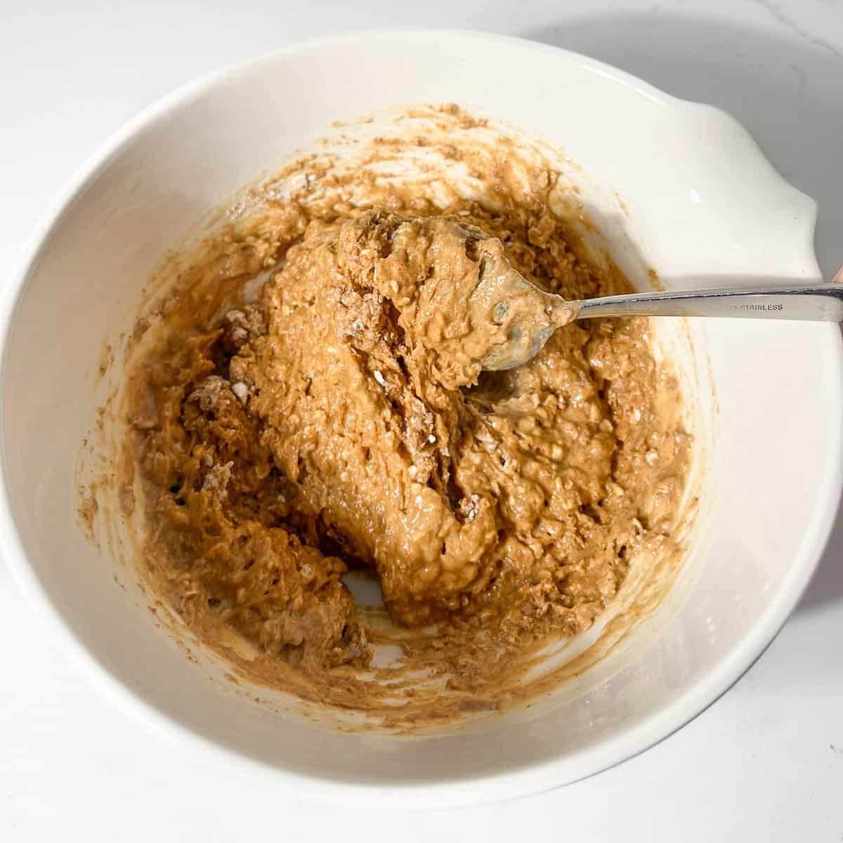 Folding the wet ingredients into the dry ingredients in a large white bowl.
