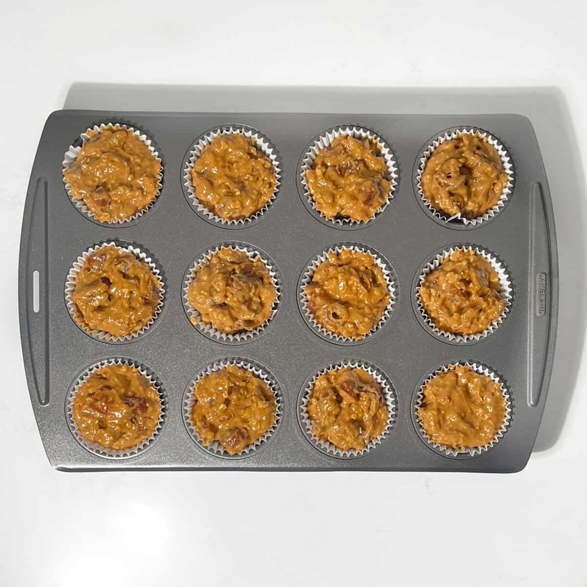 The muffin mixture scooped into muffin cases in a 12-hole muffin pan.