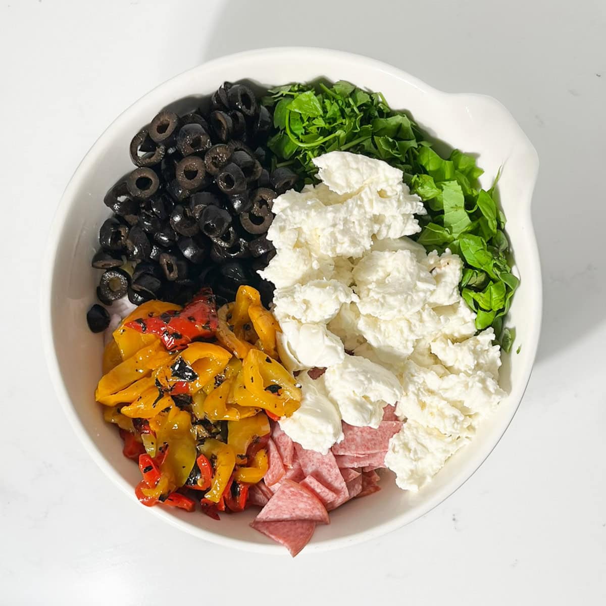 Adding all the salad-add-ins for the creamy italian pasta salad to the pasta in a large white bowl.