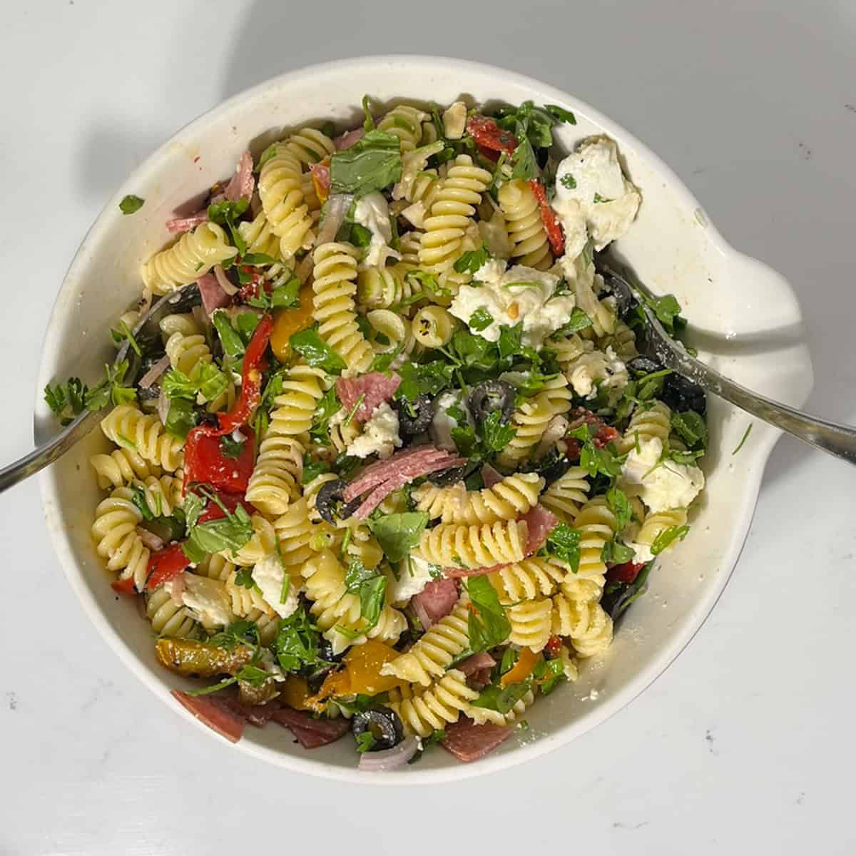 Mixing the summer pasta salad with the cooked pasta in a large white bowl.