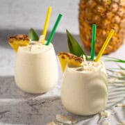 Two pina colada smoothies with a pineapple in the background.