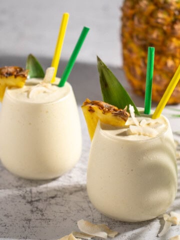 Two pina colada smoothies with a pineapple in the background.