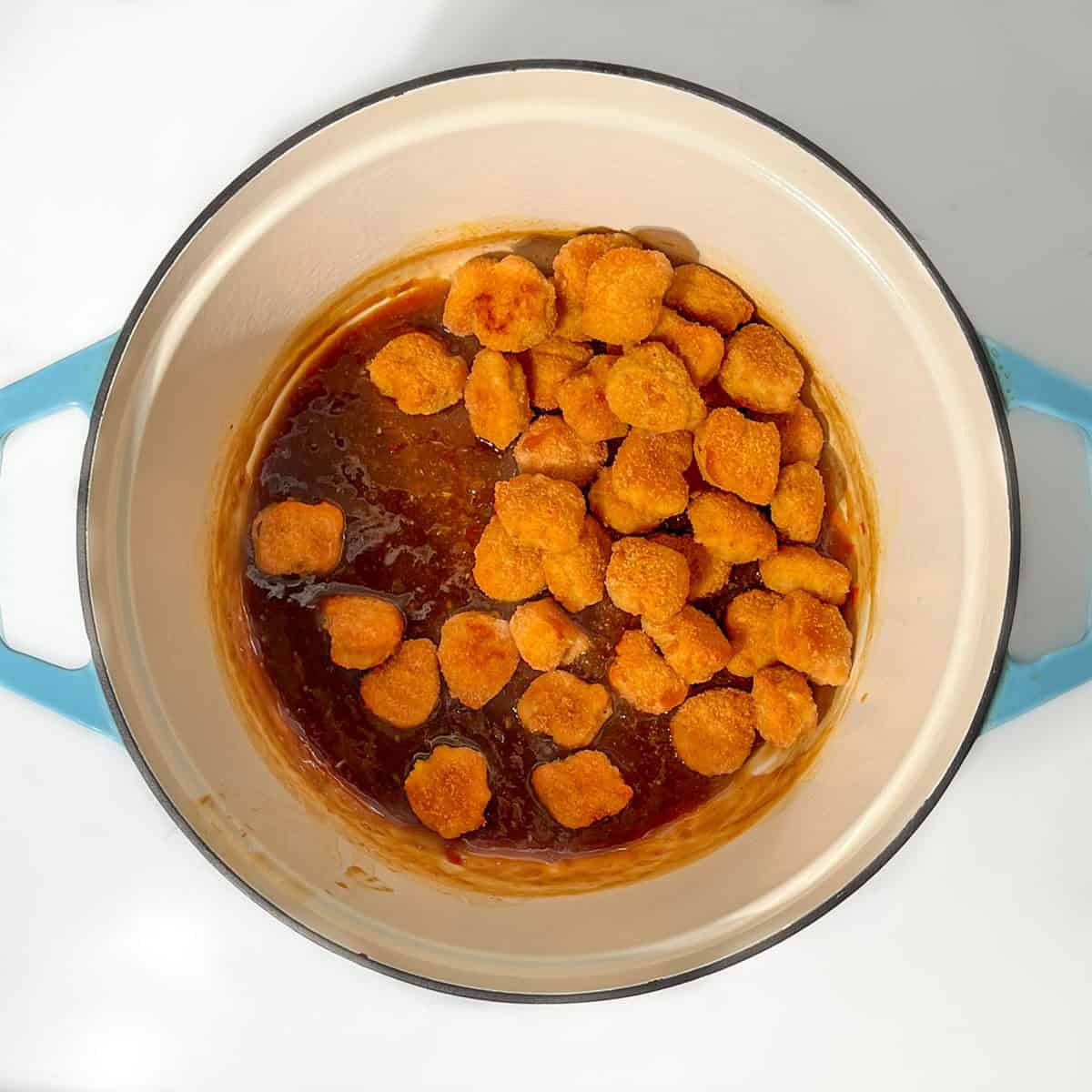 Coating the cooked chicken nuggets in the orange sauce.