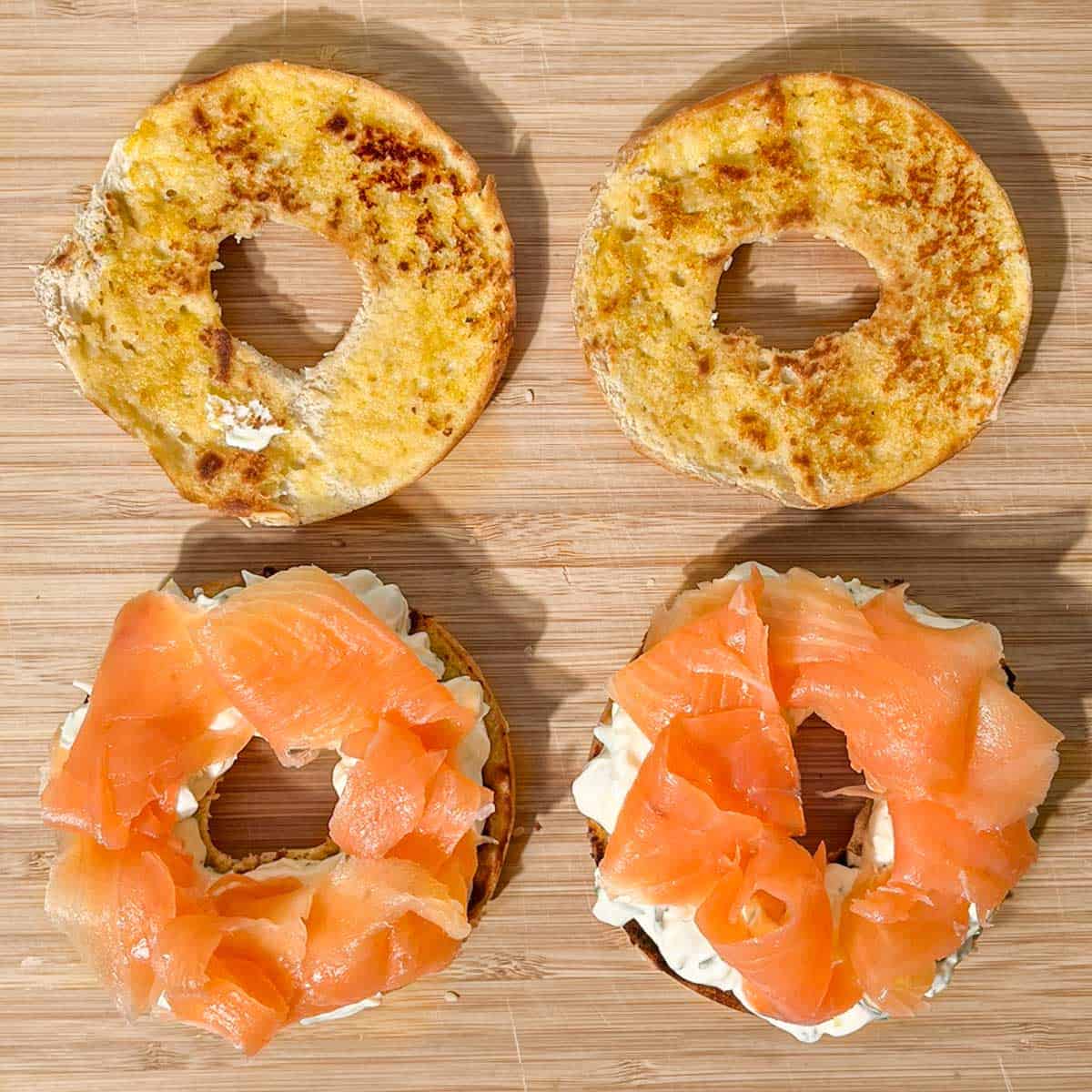 Two bagels halves layered with cream cheese and smoked salmon in a wooden board.