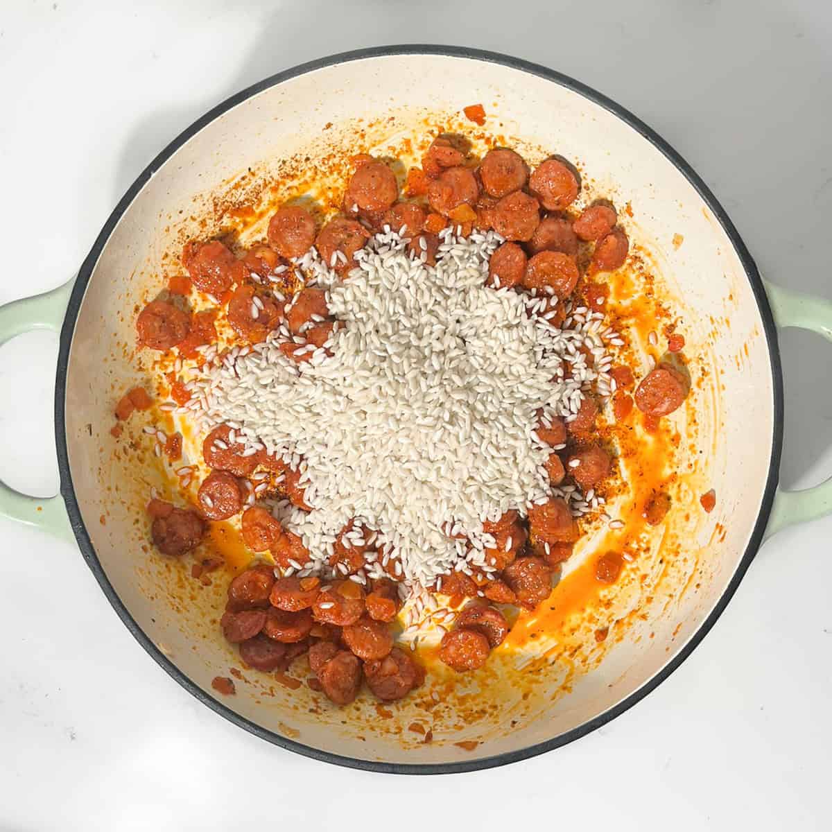 Adding risotto rice to the fried chorizo and onions in a large saucepan.