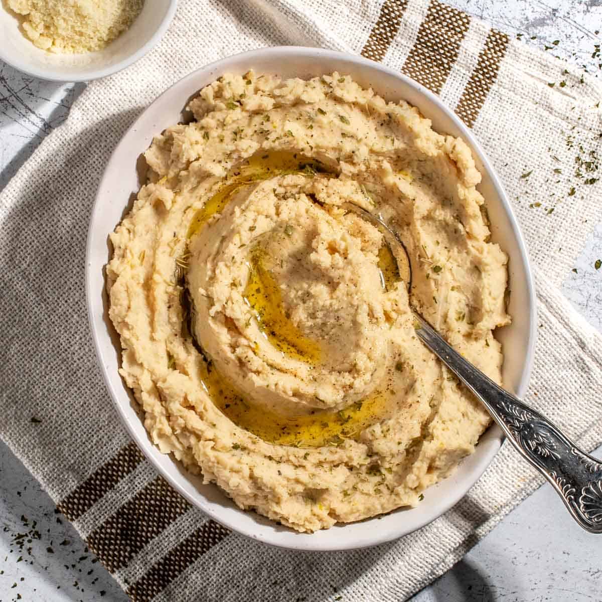 Butter bean mash in a white bowl on a neutral coloured tea towel.