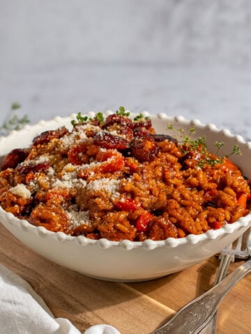 Chorizo risotto in a white bowl on a wooden board.