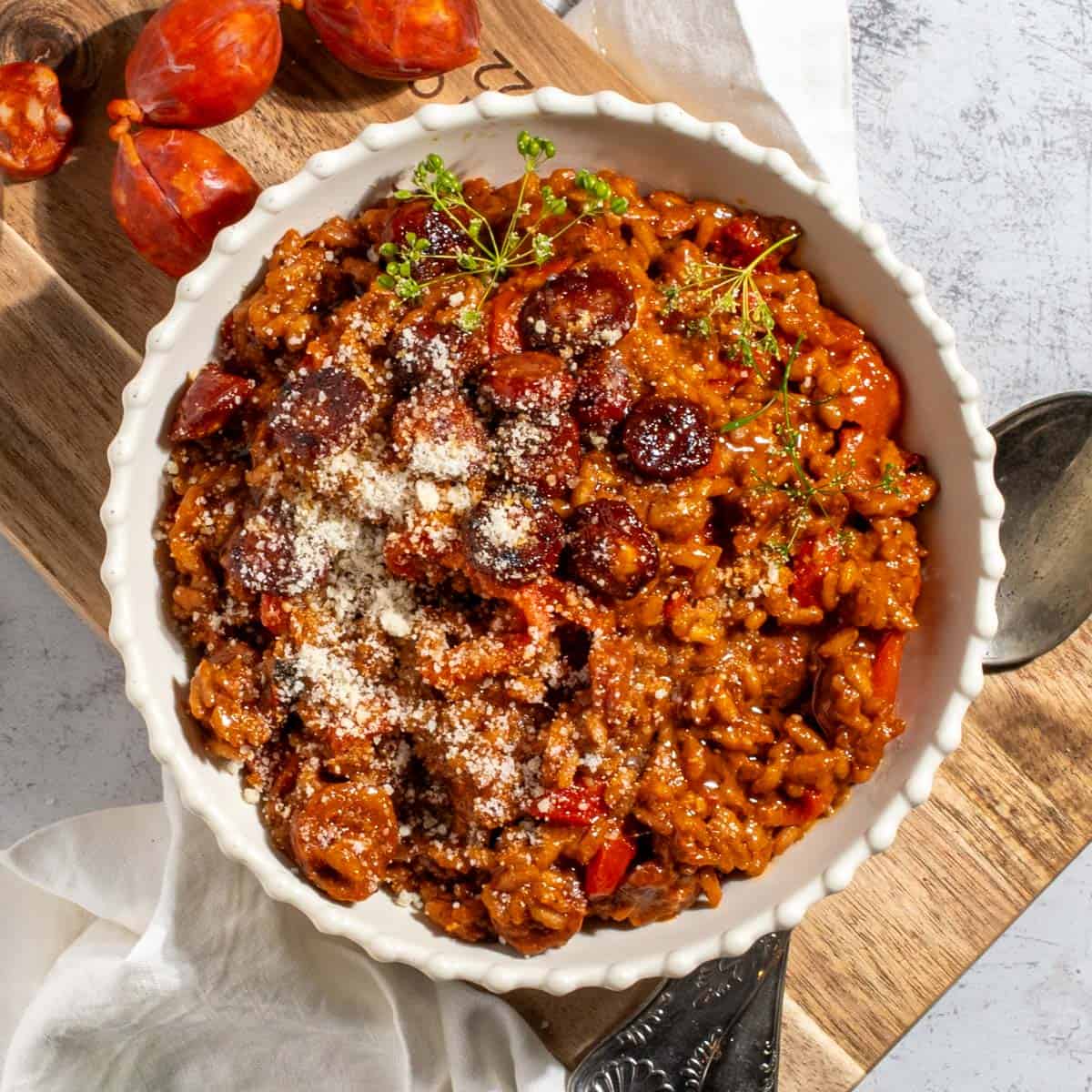 Chorizo risotto in a white bowl on a wooden board.