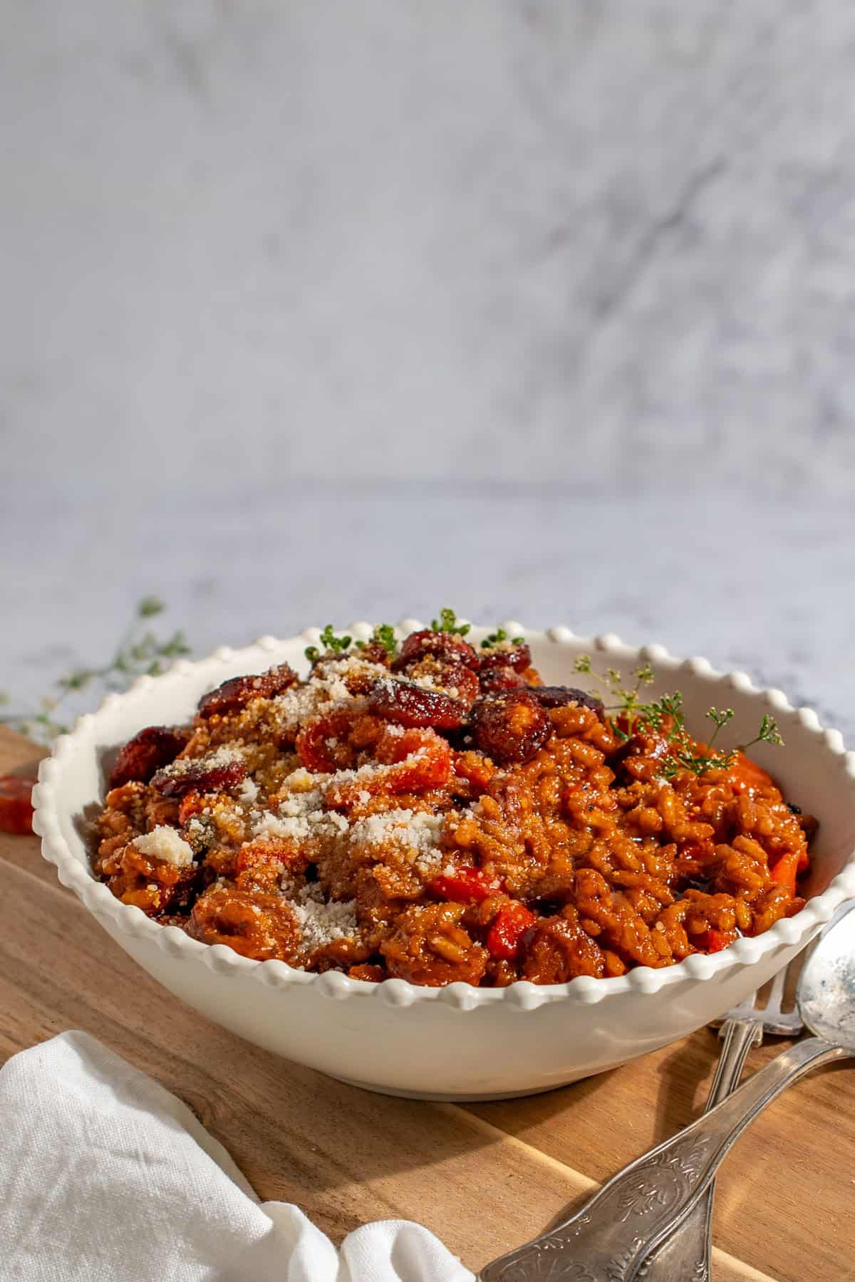 Chorizo risotto in a white bowl on a wooden board.