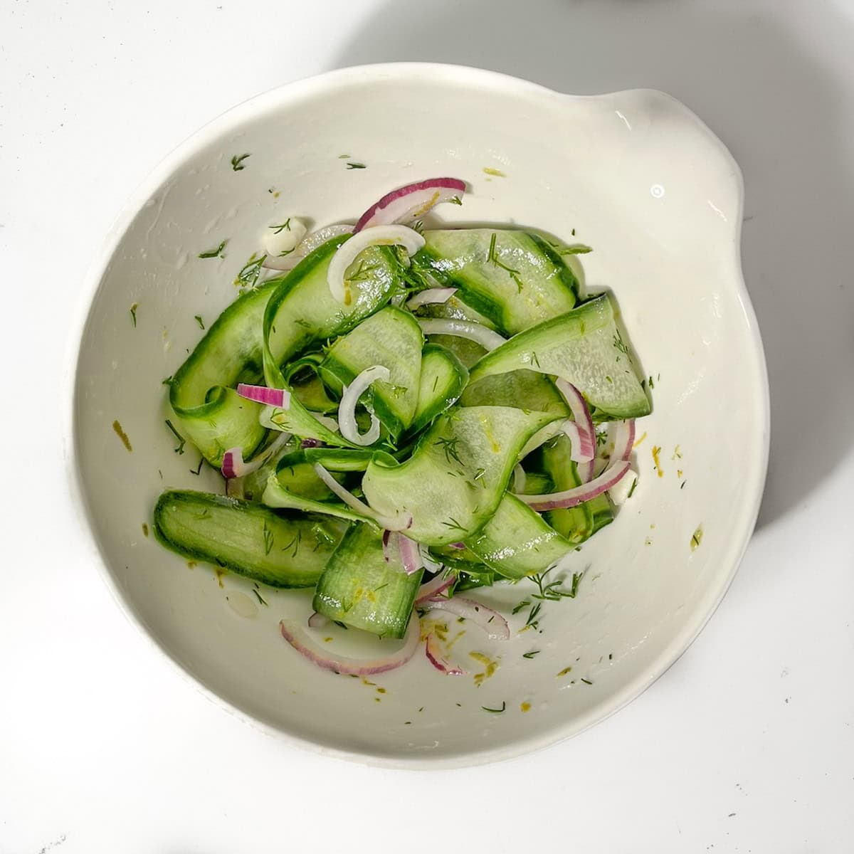 Cucumber pickle marinating in a white bowl.