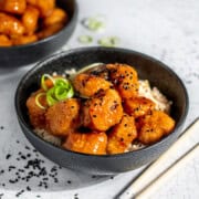Orange chicken with nuggets on a bed of rice in a black bowl.