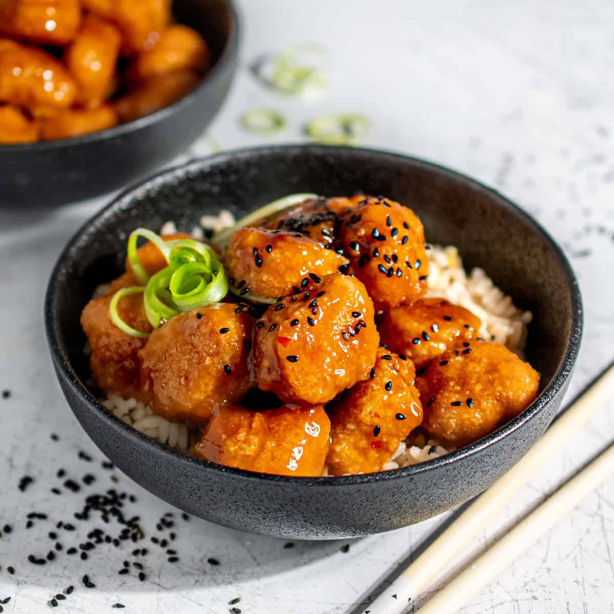Orange chicken with nuggets on a bed of rice in a black bowl.