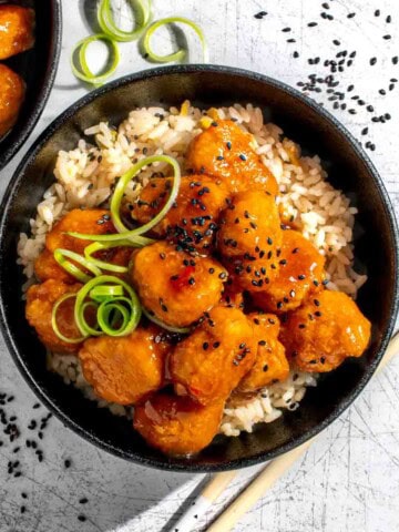 Orange chicken with nuggets on a bed of rice in a black bowl.