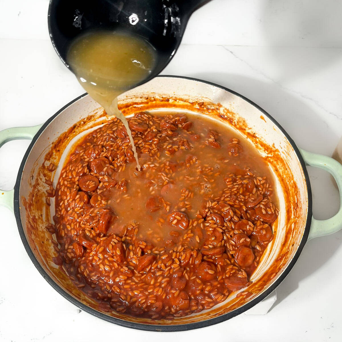 Gradually ladelling hot chicken stock into the chorizo risotto.