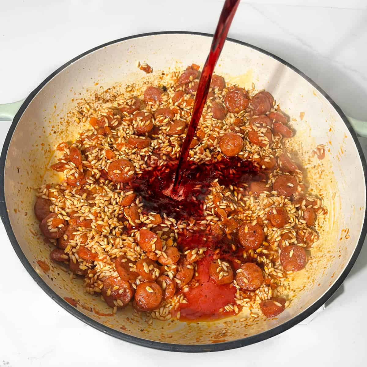 Adding dry red wine to the chorizo risotto in a large saucepan.