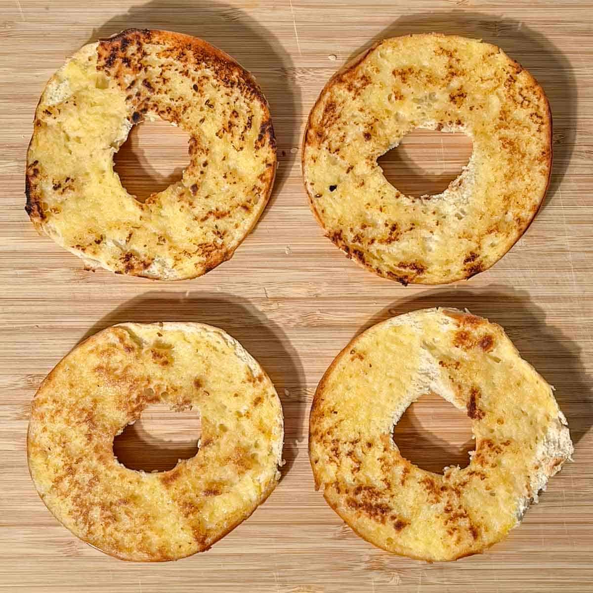 Two toasted bagels sliced in half on a wooden board.